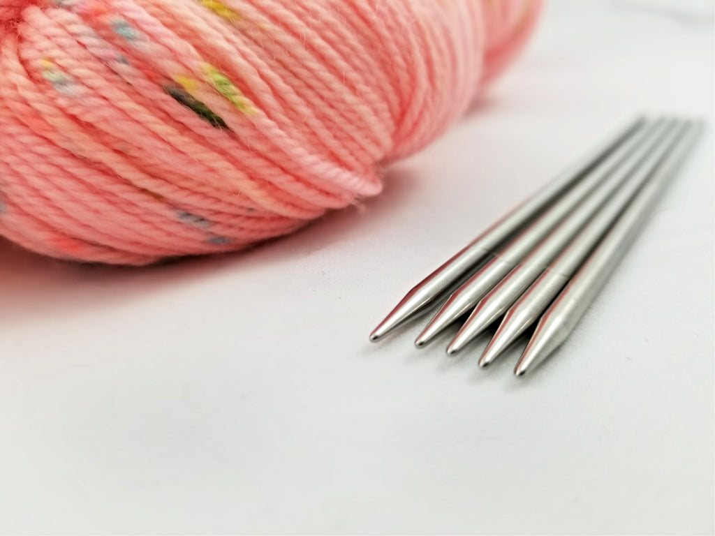 A picture of a skein of hand-dyed yarn from Lily & Pine next to a set of ChiaoGoo Stainless Steel DPNs