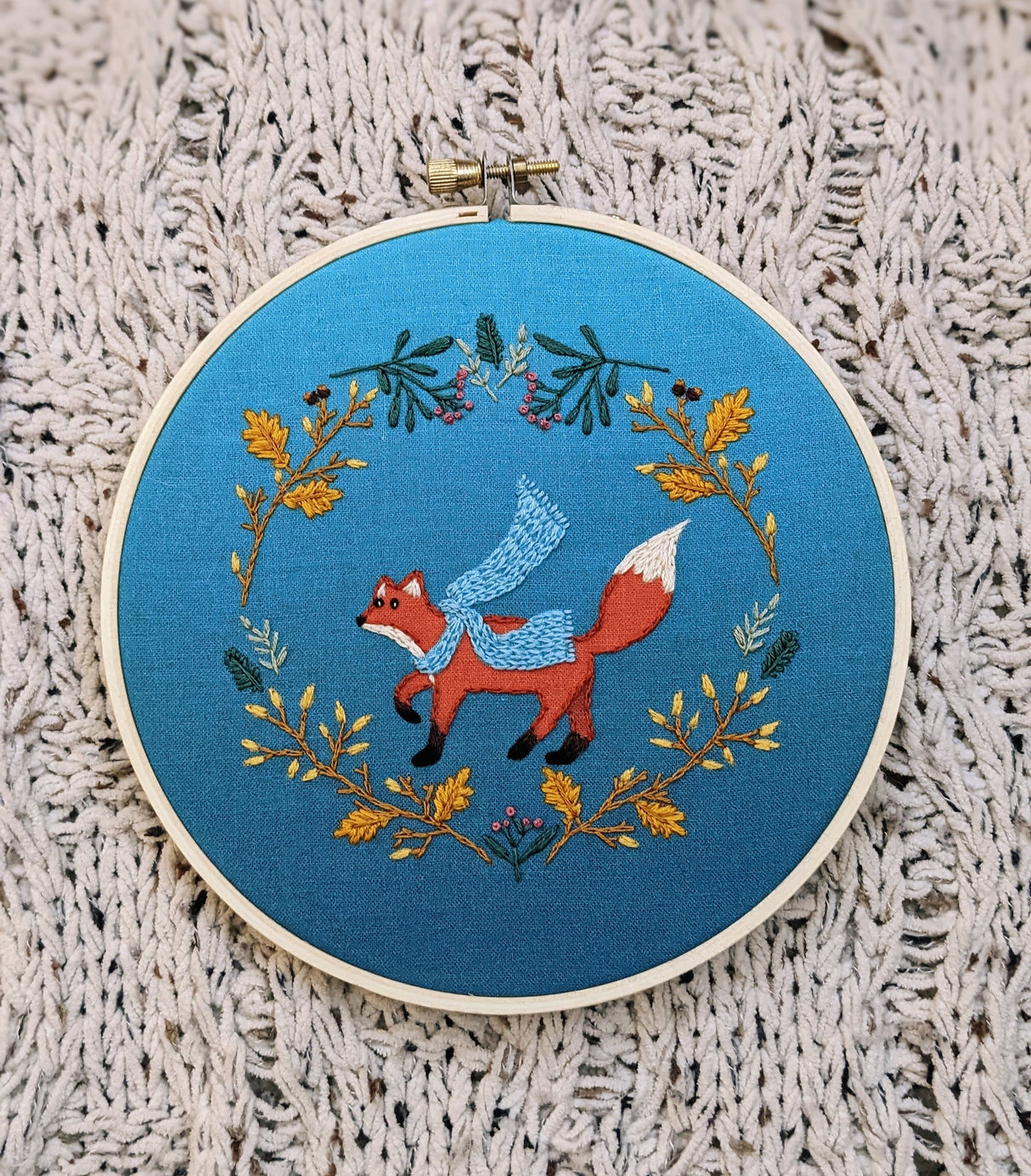 Embroidery hoop with a fox design on blue fabric against a textured beige background