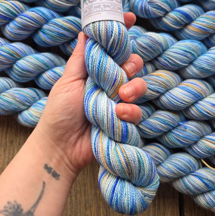 Hand holding skeins of blue and white yarn with a label on a wooden surface