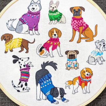 Embroidery hoop with embroidered dogs wearing colorful sweaters on a white background