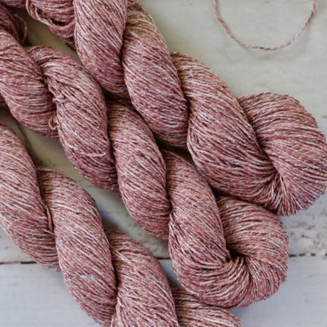 Three skeins of pink yarn on a light wooden surface