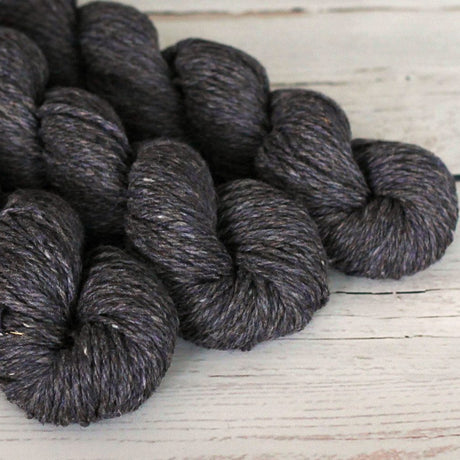 Three skeins of dark gray yarn on a light wooden surface