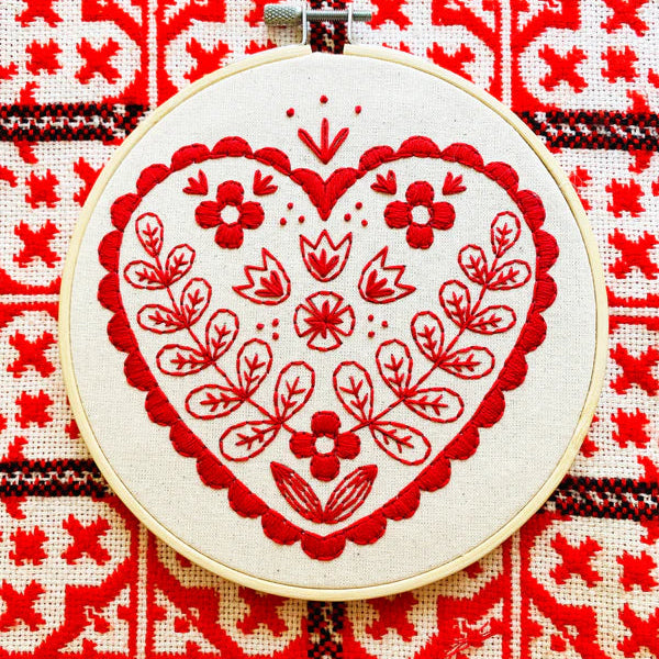 Embroidery hoop with red heart design on a red and white patterned fabric background