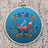 Embroidery hoop with a fox design on blue fabric against a textured beige background