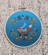 Embroidery hoop with a fox design on blue fabric against a textured beige background
