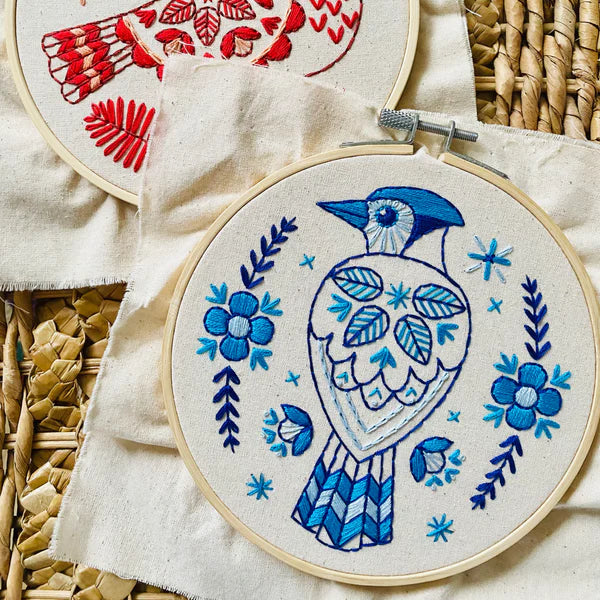 Two embroidery hoops with red and blue bird designs on a woven surface.