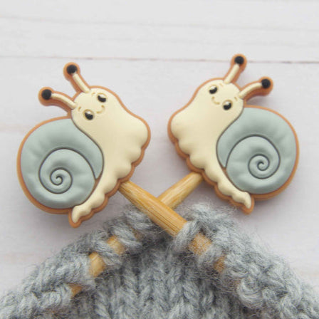 Two snail-shaped cookies on a knitting needle with gray yarn.