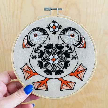 Embroidery hoop with owl design held by a hand on a wooden surface