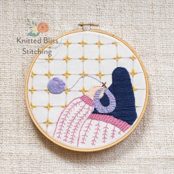 Embroidery hoop with a colorful stitched design on a beige fabric background, featuring the brand 'Knitted Bliss Stitching'.