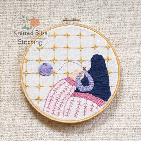 Embroidery hoop with a colorful stitched design on a beige fabric background, featuring the brand 'Knitted Bliss Stitching'.