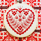 Embroidery hoop with red heart design on a red and white patterned fabric background