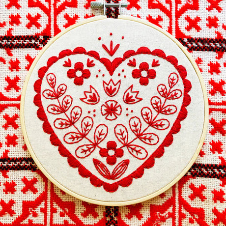 Embroidery hoop with red heart design on a red and white patterned fabric background