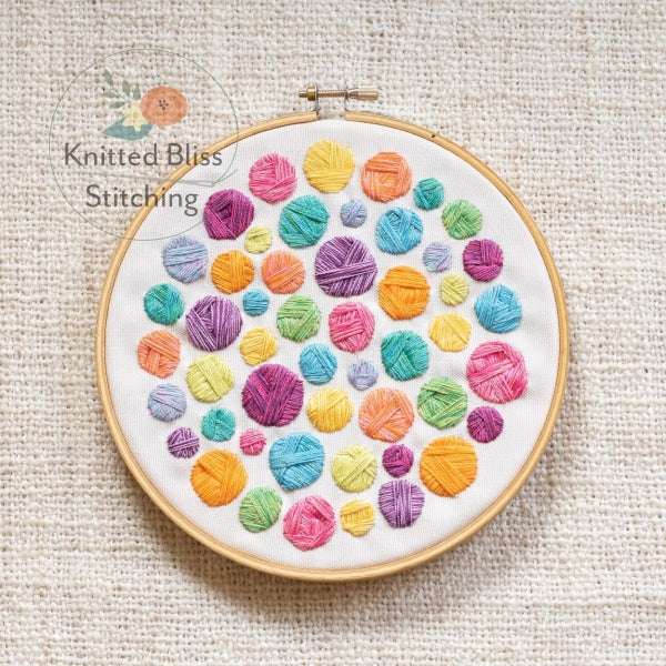 Embroidery hoop with colorful yarn ball pattern on a textured fabric background, featuring 'Knitted Bliss Stitching' logo.